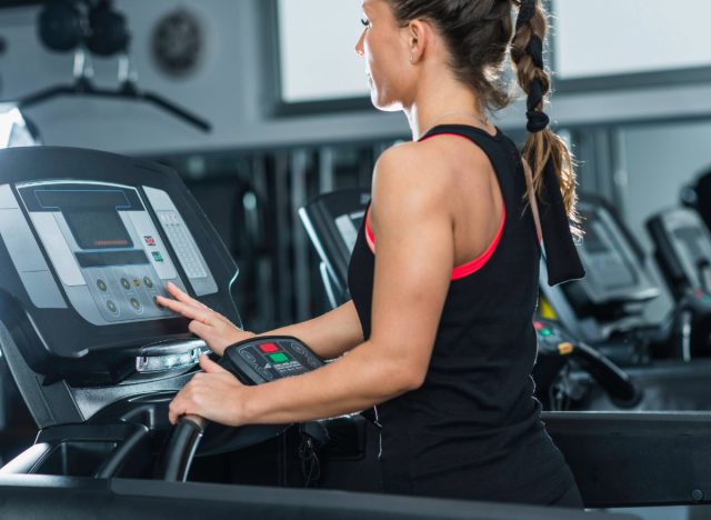 a woman adjusting a treadmill leans in the gym